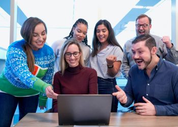 Grupo de trabalho em escritório feliz em olhando para o notebook.