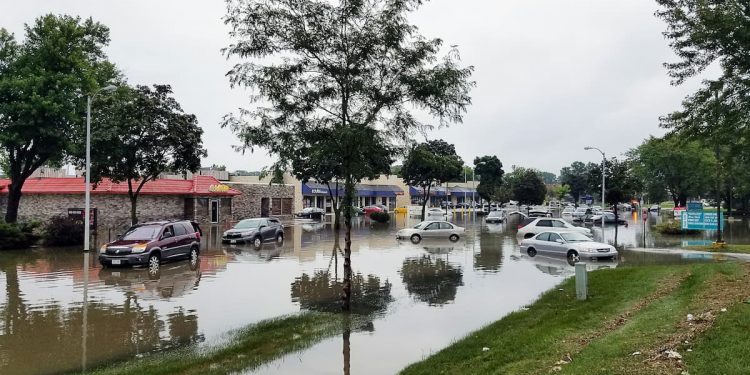 Bairro inundado de água após enchente com vários carros submersos.