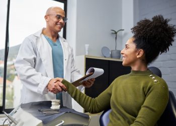 Mulher de camisa verde sentada em escritório, cumprimentando doutor de jaleco branco.
