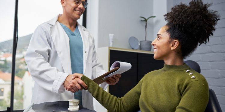 Mulher de camisa verde sentada em escritório, cumprimentando doutor de jaleco branco.