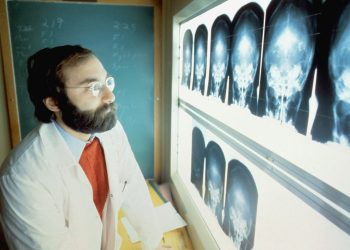 Homem de óculos vestido com avental olhando para radiografias odontológicas.