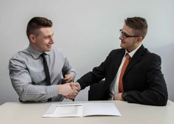Dois homens vestidos de traje social, apertando as mãos.